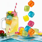 A clear glass mason jar mug filled with a yellow drink, ice cubes, a pink-and-white striped straw, and mint leaves, shown with colorful translucent ice cubes floating and splashing around it against a white background.